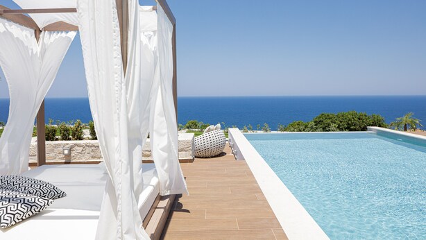 Un espace aménagé au bord de la piscine, avec vue sur l’océan, un auvent blanc et une terrasse carrelée.