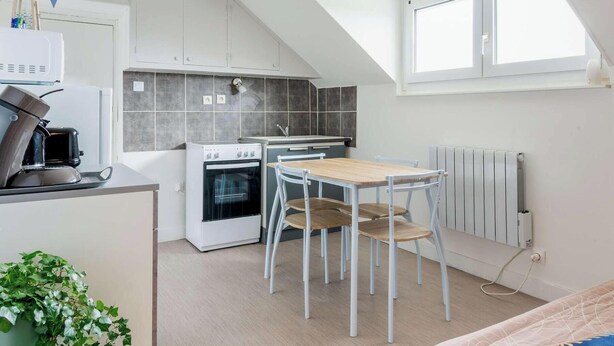 A compact kitchen with a stove, oven, and sink, a small dining table with chairs, and a view of the sea. - Apartment 300m from the beach - Shared outdoor area (Asnelles)