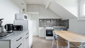 A modern kitchen with white cabinets, a microwave, a kettle, a toaster, and a wooden dining table. - Apartment 300m from the beach - Shared outdoor area (Asnelles)