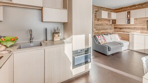 A modern kitchen with built-in appliances, a grey sofa, and a wooden accent wall. - Renovated apartment for 4, lake view, hotel services (Tignes)