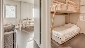 A modern, minimalist room with a bunk bed, a dining area with a table and chairs, and a view of a snowy landscape through a window. - Renovated apartment for 4, lake view, hotel services (Tignes)