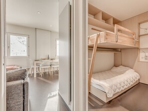 Une chambre moderne et minimaliste, dotée d’un lit superposé, d’un coin repas avec une table et des chaises, et offrant une vue sur un paysage enneigé par la fenêtre.