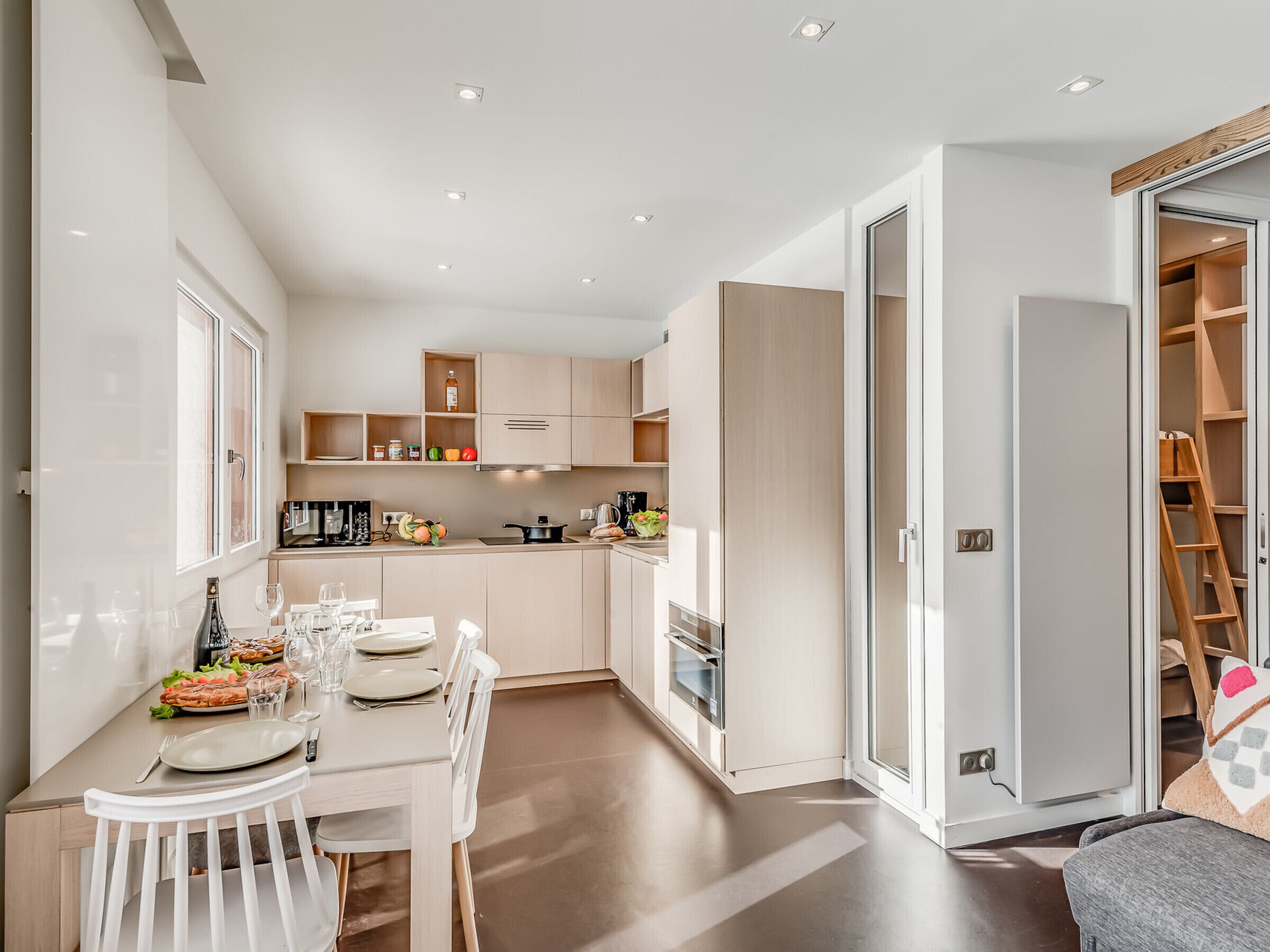 A modern kitchen with white cabinetry, a dining table set for four, and a sliding glass door leading to a storage area.