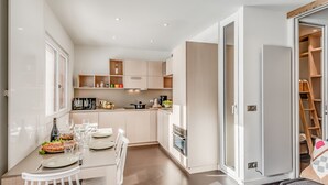 A modern kitchen with white cabinetry, a dining table set for four, and a sliding glass door leading to a storage area. - Renovated apartment for 4, lake view, hotel services (Tignes)
