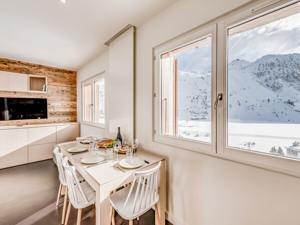 Une cuisine moderne agrémentée d’éléments en bois, un coin repas avec des meubles blancs et de grandes fenêtres offrant une vue sur les montagnes.