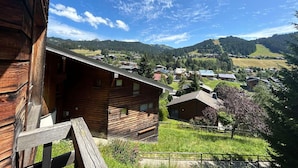 A wooden cabin with a balcony overlooking a valley with houses and mountains. - Renovated Apartment, Walking Distance to Slopes, South-West Balcony, Comfort Amenities (Les Gets)