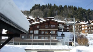 A snow-covered ski resort with wooden buildings, a ski lift, and a clear sky. - Renovated Apartment, Walking Distance to Slopes, South-West Balcony, Comfort Amenities (Les Gets)