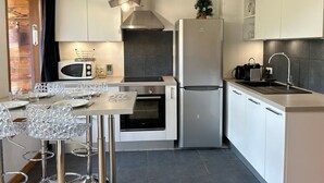 A modern kitchen with white cabinets, a stainless steel refrigerator, a microwave, and a dining area with a glass table and chairs. - Renovated Apartment, Walking Distance to Slopes, South-West Balcony, Comfort Amenities (Les Gets)