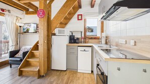 Eine kompakte Küche mit Mikrowelle, Kaffeemaschine und Spüle. Eine Holztreppe führt zu einer Sitzecke mit Blick ins Freie.