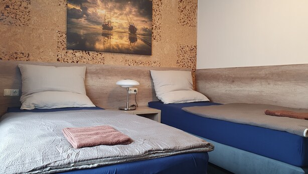 Ett hotellrum med två sängar, en målning som föreställer båtar på vattnet och en vägg med trästruktur.