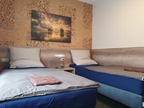 A room with two beds, a painting on the wall, and a nightstand with a lamp.