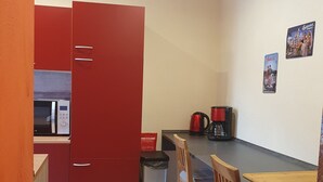 Ett kompakt kök med ett rött skåp, en kaffebryggare och en papperskorg.
