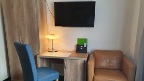 Ett litet, möblerat rum med ett skrivbord, en stol, en tv och en lampa.