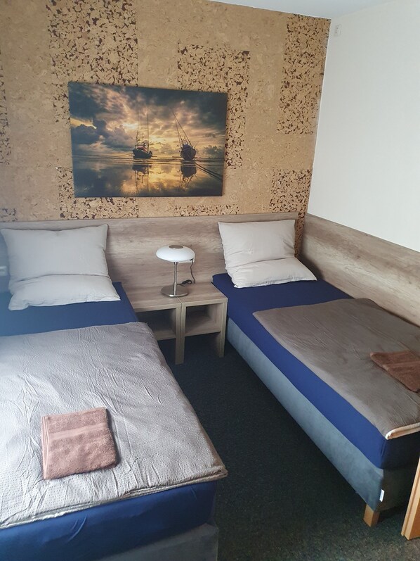 A room with two beds, a small table, and a painting of boats on water.