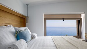 A bedroom with a large window offering a view of the sea, a neatly made bed with white linens, and a wooden headboard. - Perfect Hideaway for Families & Unmatched Sunsets (Rethymno)
