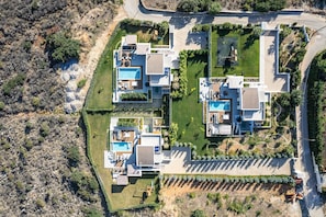 Un complexe résidentiel moderne comprenant plusieurs maisons, chacune dotée d’une piscine, d’un espace extérieur aménagé et d’un jardin bien entretenu.
