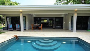 Ein moderner Poolbereich im Freien mit Essbereich und einer überdachten Terrasse.