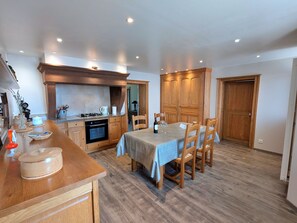 A compact kitchen with wooden cabinets, a dining table with four chairs, and a built-in oven. - Charming Cottage Near Abbey, Perfect for History Lovers & Nature Enthusiasts - Sleeps 5 (Étival-Clairefontaine)