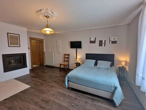 A bedroom with a bed, a chair, a television, and a fireplace. - Charming Cottage Near Abbey, Perfect for History Lovers & Nature Enthusiasts - Sleeps 5 (Étival-Clairefontaine)