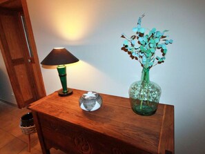 Ein Nachttisch aus Holz mit einer grünen Lampe, einer dekorativen Glasvase mit blauen Blumen und einem kleinen Korb.