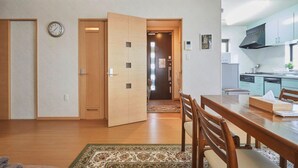 Un salon moderne avec un plancher en bois, une table à manger avec des chaises, un coin cuisine doté de placards et d’appareils électroménagers, et une horloge au mur.
