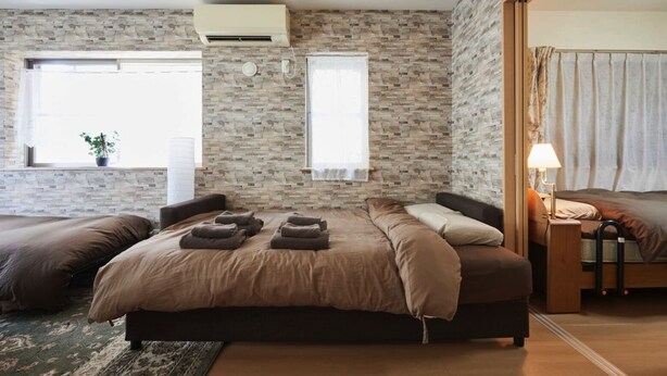 Une chambre avec un mur en pierre, un grand lit avec de nombreux oreillers, une table de chevet avec une lampe et une fenêtre avec des rideaux.