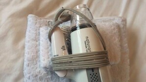 Un appareil portatif doté d’une sangle flexible pour le cou, qui pourrait être un appareil de massage personnel, posé sur une serviette blanche.
