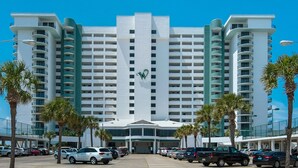 A multi-story hotel with a prominent 'W' logo, featuring a central entrance, parking lot, and palm trees.