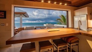 Una cocina moderna con un amplio ventanal con vistas al océano, encimera de madera y taburetes de bar.