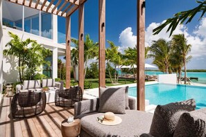 A poolside area with outdoor furniture, a view of the ocean, and palm trees. - Villa Cabuya | Contemporary Beachfront Luxury in Blue Cay Estate (Leeward Settlement)