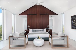 Ein modernes Schlafzimmer mit einem großen Bett, zwei Sesseln, einem Couchtisch und einem Deckenventilator.