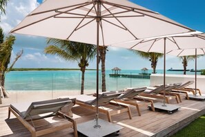 A poolside area with lounge chairs and umbrellas, overlooking a clear blue sea. - Villa Cabuya | Contemporary Beachfront Luxury in Blue Cay Estate (Leeward Settlement)