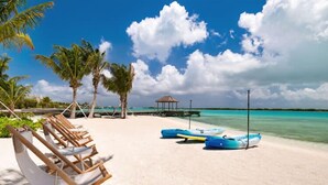 Ein Strand mit Liegestühlen, einer Laube und blau lackierten Wasserfahrzeugen.