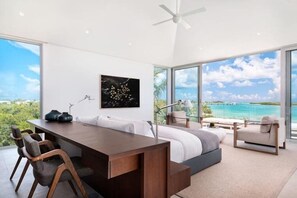 Quarto moderno com uma cama grande, uma escrivaninha e vista para o oceano.