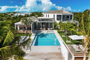 Ein modernes Haus mit Swimmingpool, umgeben von Palmen und blauem Himmel.