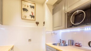 A kitchen with white tiles, a stainless steel sink, a dishwasher, and a microwave.