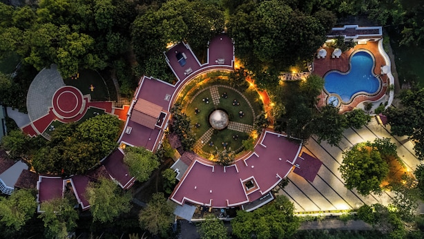 An aerial view of a resort with a central circular courtyard, surrounding buildings, and a swimming pool.