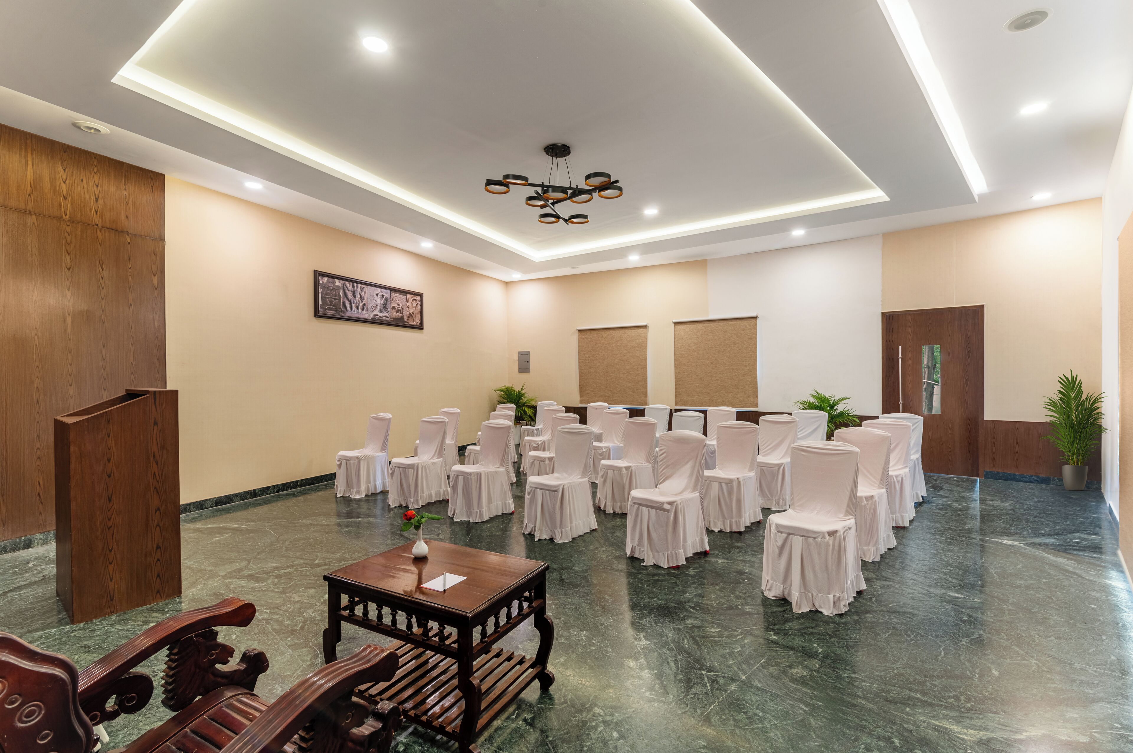 Une salle de conférence avec des rangées de chaises recouvertes de tissu blanc, un pupitre en bois et une table sur laquelle est posé un vase.