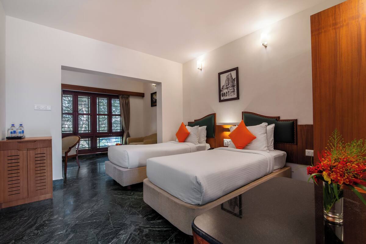 Ein Hotelzimmer mit zwei Betten, einem Holztisch, einem Stuhl und Blick ins Freie durch große Fenster.