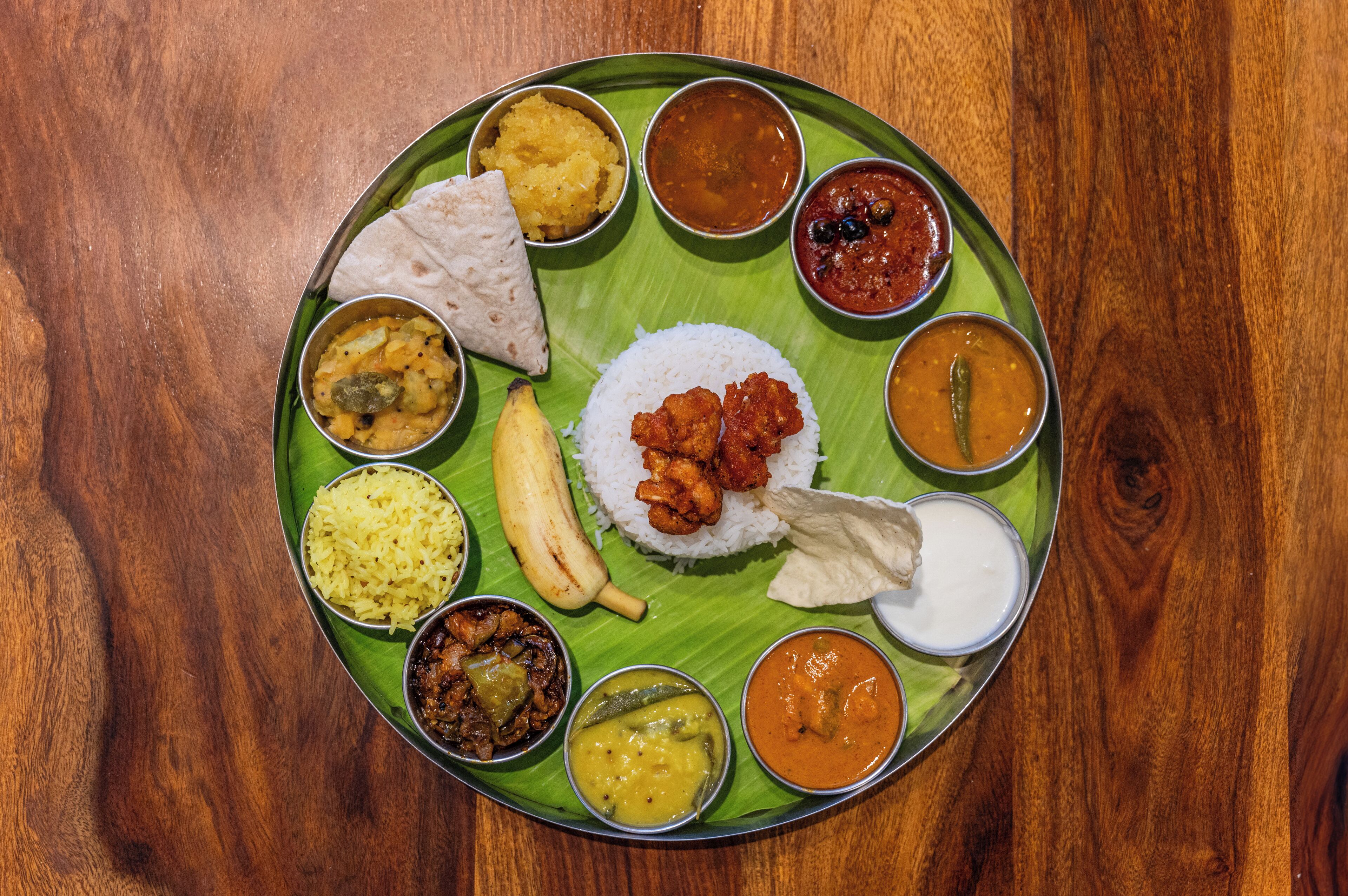 A plate of Indian cuisine with rice, various curries, and a banana on a banana leaf.