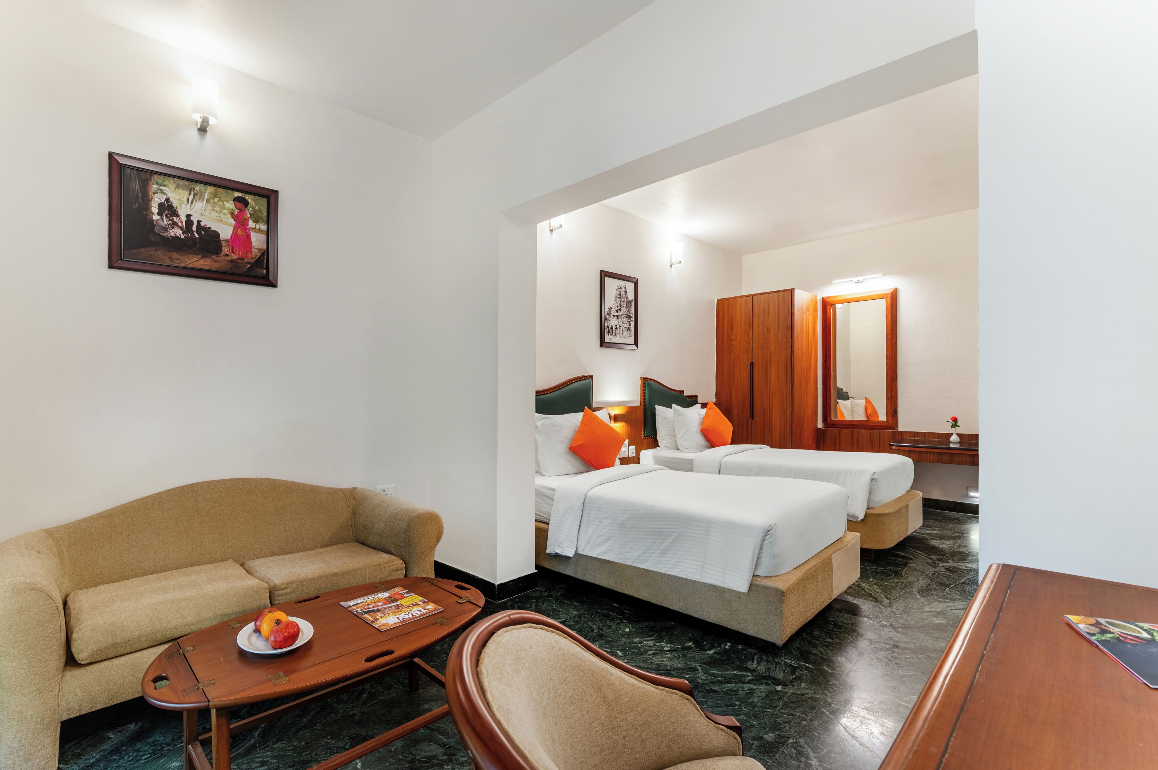 A hotel room with a sofa, two beds, a wooden coffee table, and a framed picture on the wall.