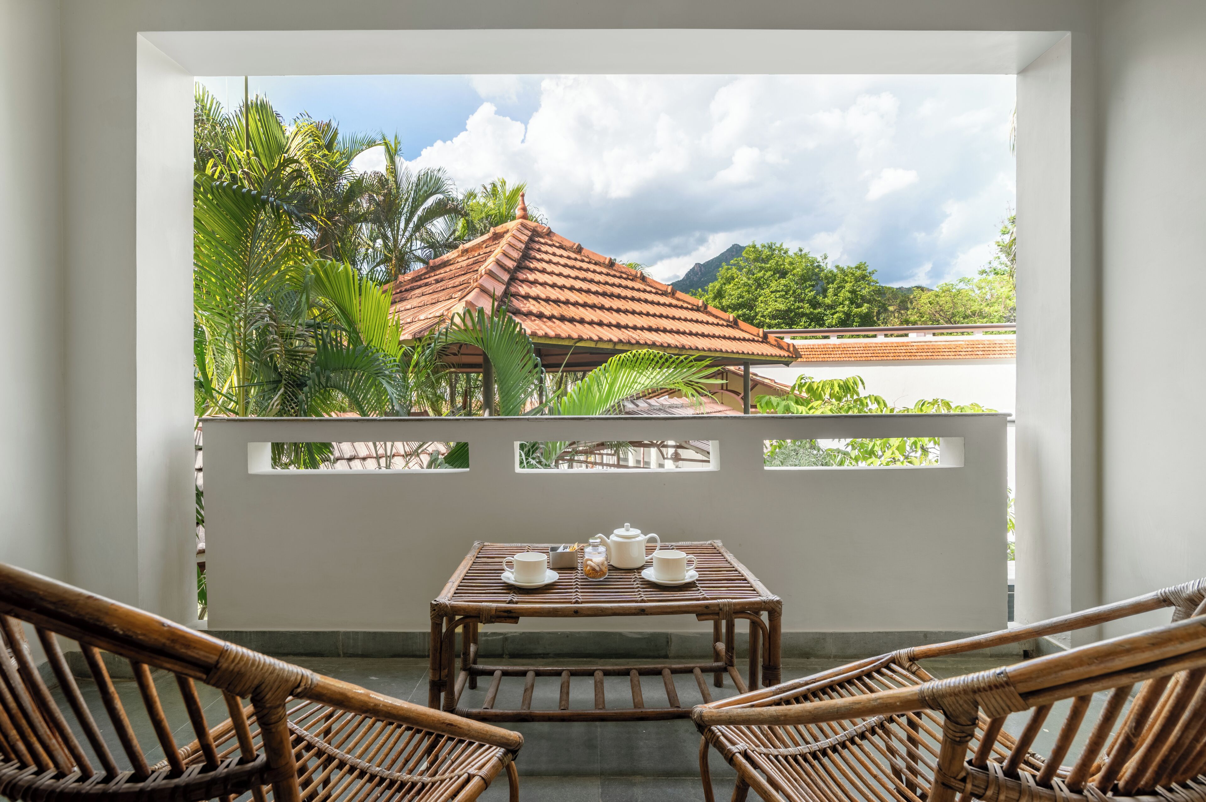 Ein Balkon mit Tisch, der für Tee gedeckt ist, Korbstühle und Blick auf ein traditionelles Haus mit Ziegeldach.