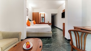 A hotel room with a bed, a wooden desk, a chair, a sofa, and a fruit plate on the desk.