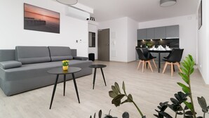 Una sala de estar moderna con un sofá gris, dos mesas negras y un comedor con sillas negras y una mesa blanca.