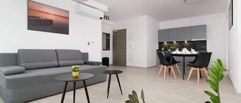 Una sala de estar moderna con un sofá gris, dos mesas negras y un comedor con sillas negras y una mesa blanca.