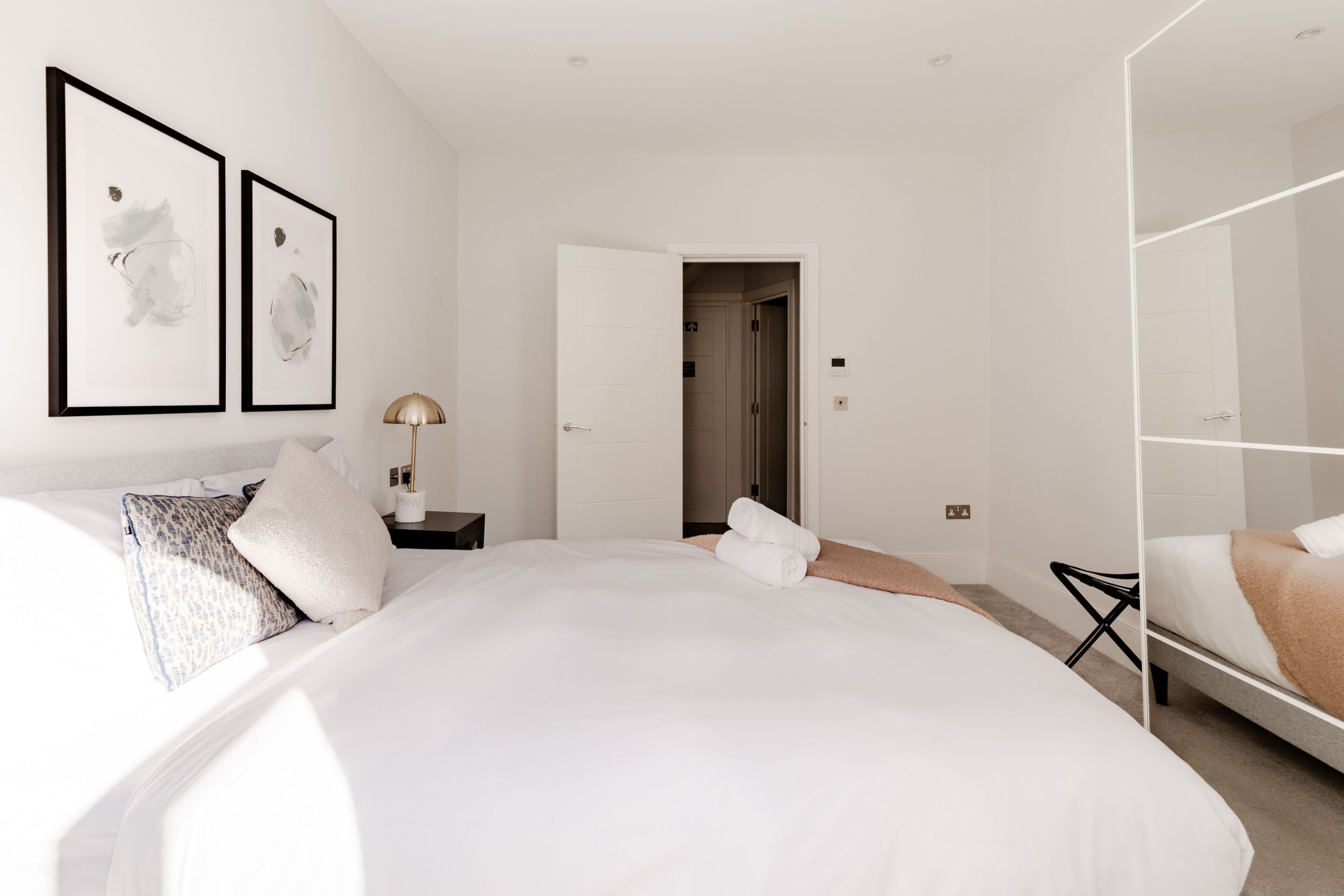 A modern hotel room with a large bed, a bedside table with a lamp, and a wardrobe.