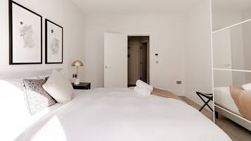 A modern hotel room with a large bed, a bedside table with a lamp, and a wardrobe.