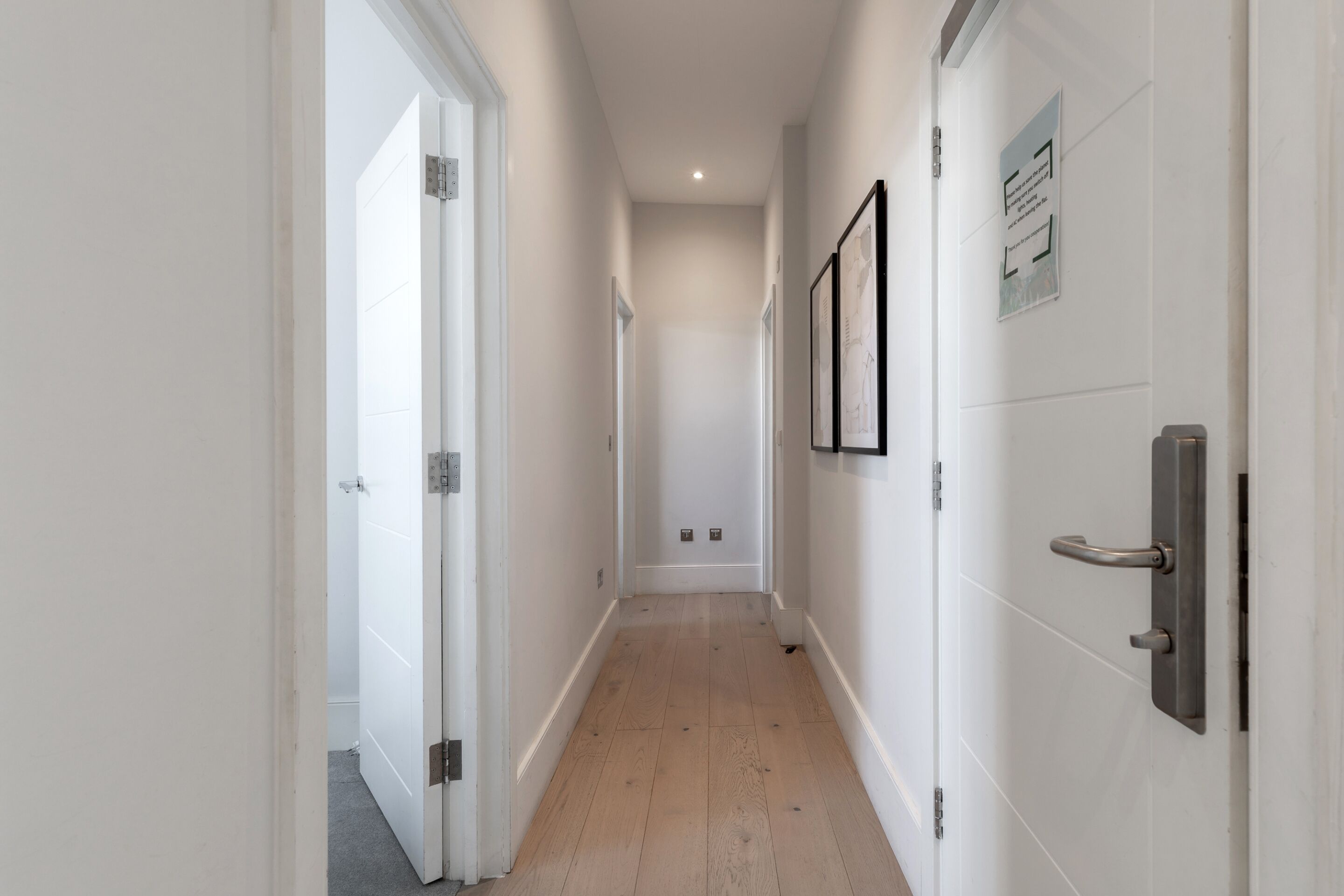 Un couloir étroit aux murs blancs, doté d’un plancher en bois et d’une porte située sur le côté droit.