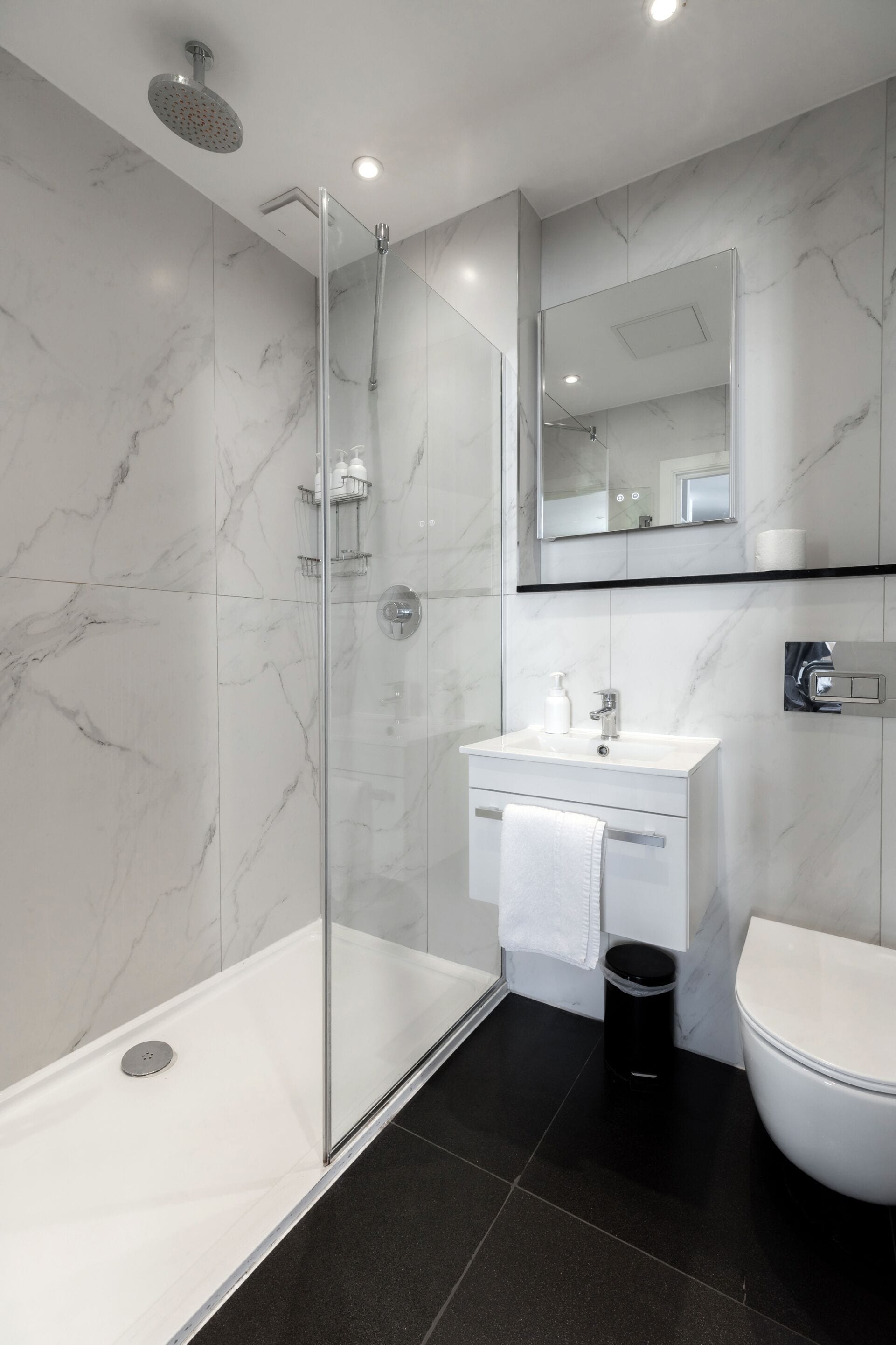 Un baño moderno con ducha acristalada, lavabo blanco y retrete.