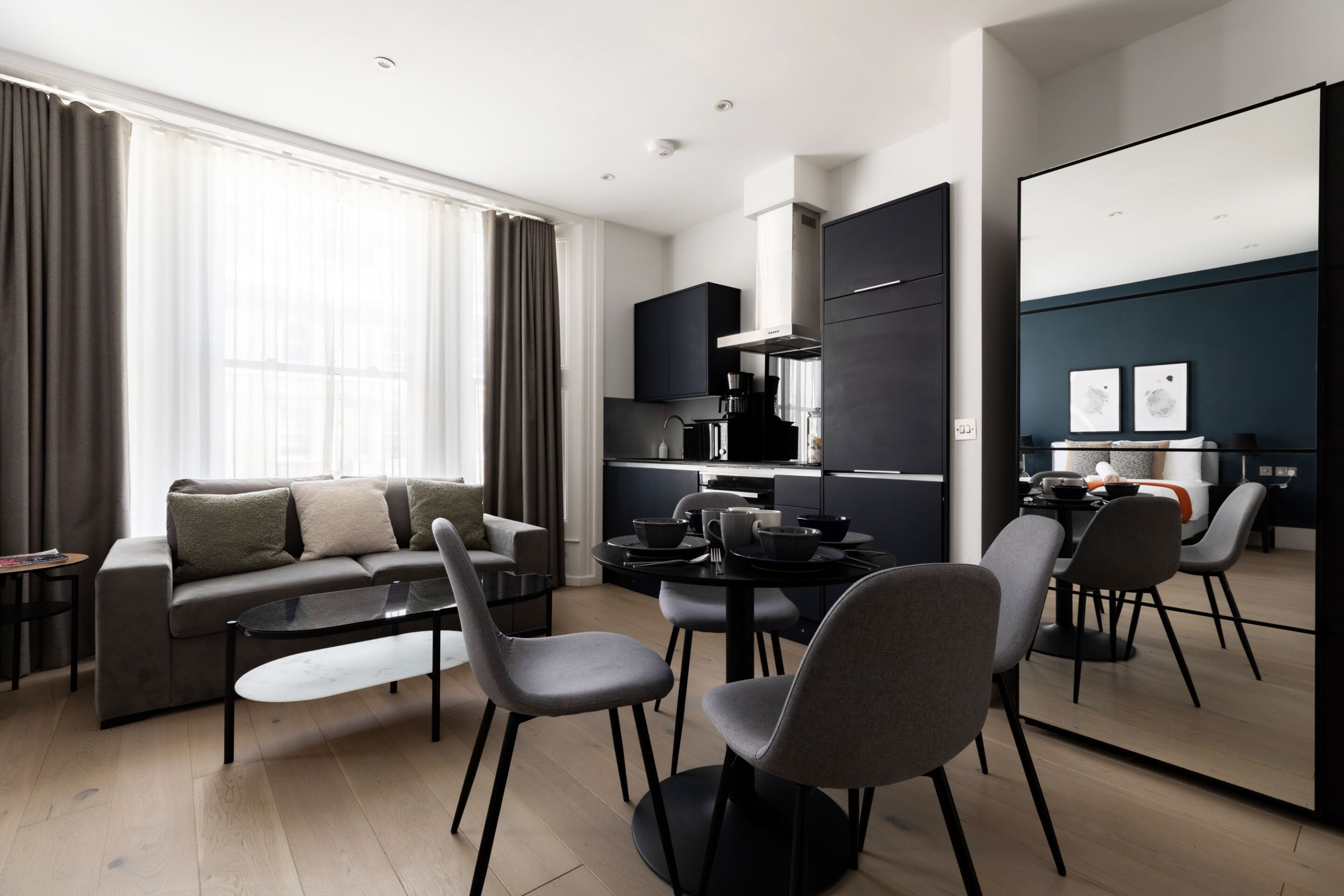 A modern living room with a sofa, coffee table, and chairs, a kitchen area with cabinets and appliances, and a dining area with a table and chairs.
